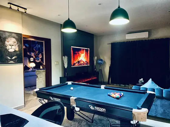 Games lounge with a blue pool table, green pendant lamps, lion portrait and an electric fireplace.