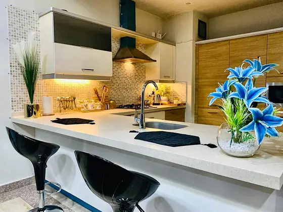 Kitchen with breakfast bar, black stools, fresh blue lilies, gas hob and chimney.