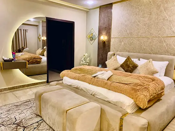 Bed with upholstered ottomans beside an arched mirror reflecting the room.