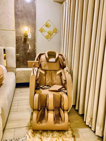 Full-body massage chair with armrest controls beside the bedroom curtains.
