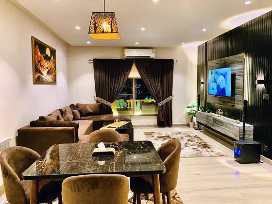 Living room with a chocolate velvet sectional, marble-top dining table, wall-mounted TV with wall lights, subwoofer and desert-landscape art.