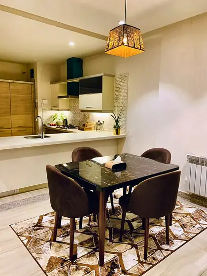 Dining table with velvet chairs and a patterned rug in front of the kitchen.