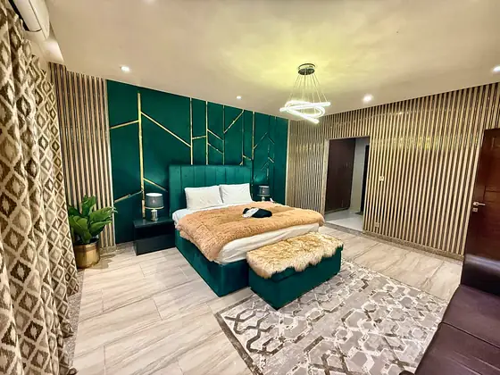 The bedroom from the window side: slatted wood panels, patterned curtains and an emerald footboard.