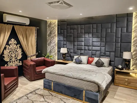 Bedroom with a grey padded-panel headboard, blue velvet footboard with gold trim, leather armchairs, twin lamps and AC.