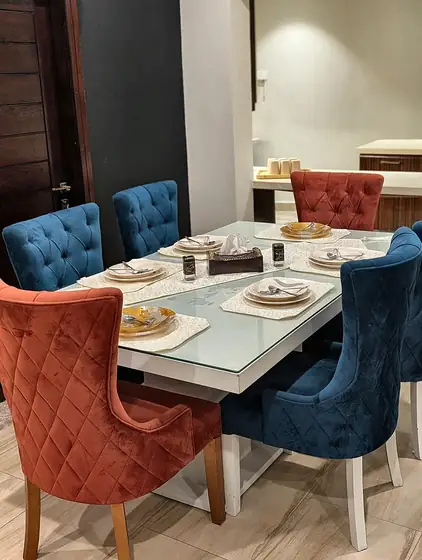 Dining table with glass top and velvet chairs in rust and navy, laid for a meal.