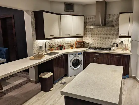 Kitchen with a breakfast island, gas hob, chimney, built-in washing machine and waste bin.