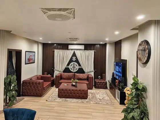 Living and dining overview with wall clock, ceiling AC and indoor plants.