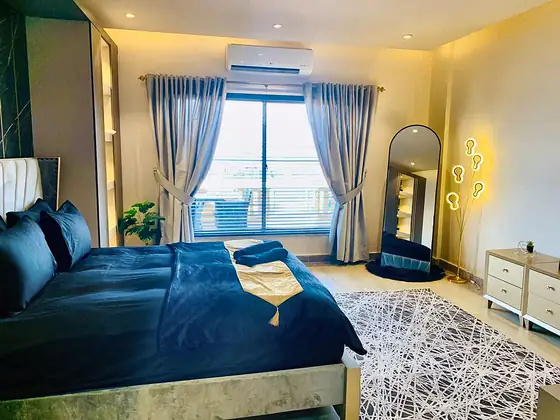 Bedroom with navy bedding, window curtains, arched mirror, floor lamp and chest of drawers.