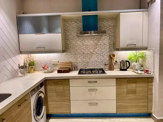 Kitchen with wood-grain and white cabinets, gas hob, chimney, kettle and washing machine.