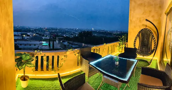 Terrace at dusk: glass-top rattan dining set, hanging egg chair, LED-lit turf and a wide view over the city.