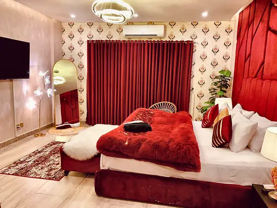 Bedroom with wall-mounted TV, full-length gold-framed mirror, designer floor lamp and crimson blackout curtains.
