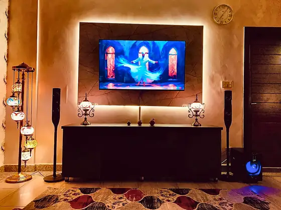 TV wall with warm LED backlight, mosaic table lamps, floor-standing speakers and subwoofer.