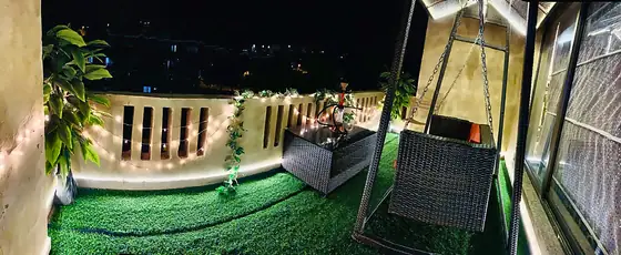 Private terrace with artificial-turf lawn, fairy lights, climbing greenery and a covered swing seat.